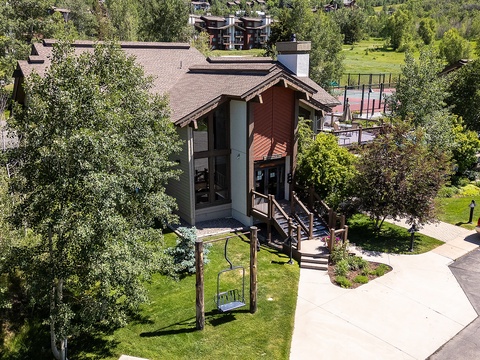 Aerial view of a charming mountain-style vacation rental surrounded by lush greenery and nearby recreational facilities including tennis courts.