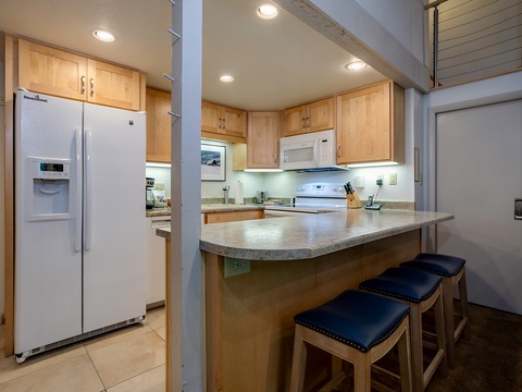 Gather around the breakfast bar in your fully equipped kitchen, where warm wood cabinetry, ample counter space, and modern appliances make meal prep easy and enjoyable during your stay.