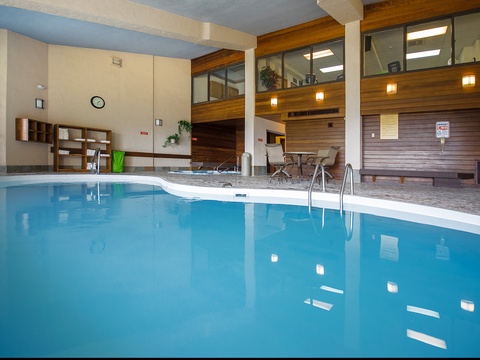 An inviting indoor pool surrounded by warm wood accents, with poolside seating and upper-level viewing areas for a relaxing swim experience.