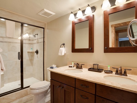 Your private bathroom features a spacious dual-sink vanity, walk-in shower, and warm wood finishes for a relaxing retreat after your day.
