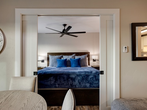 Step into your serene bedroom retreat with a plush bed dressed in rich blue linens, gentle bedside lighting, and a quiet ceiling fan to keep you comfortable all night.