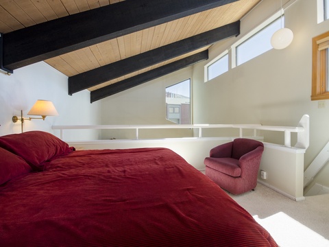 Your loft-style bedroom features soaring wood-beamed ceilings, crisp natural light, and rich red linens that invite cozy mountain evenings after adventures.