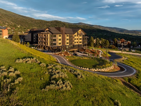 The property sits nestled among forested mountain slopes, with a winding access drive leading through landscaped grounds to the multi-story main building.