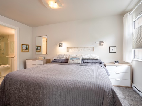 Your serene bedroom retreat features a plush queen bed with reading lights, bedside storage, and natural light streaming through the window. The ensuite bathroom is just steps away for your convenience.