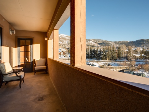 Balcony with chairs frames a snow-capped mountain view and evergreen-dotted landscape, creating a peaceful alpine setting for your mountain retreat.