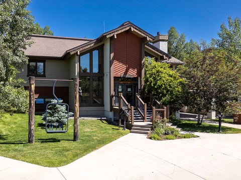 Modern mountain retreat featuring natural wood siding and expansive windows, nestled among mature trees with well-maintained landscaping and convenient driveway access.