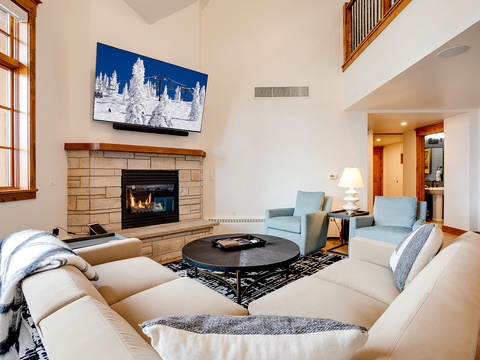 Settle into your cozy living room where a stone fireplace crackles warmth and vaulted ceilings create an airy, inviting space perfect for relaxing after mountain adventures.