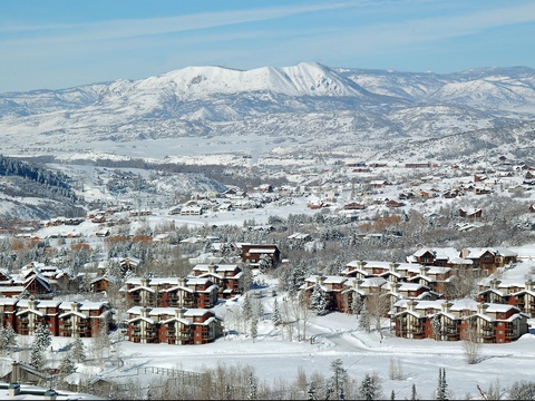 Elevated view of a mountain resort community nestled in a snow-covered valley with majestic peaks rising in the background. Seasonal winter landscape showing the property's natural alpine setting.