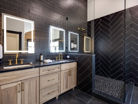 Step into your luxurious ensuite with striking herringbone tile walls, dual vanities with gold fixtures, and a modern walk-in shower featuring elegant mosaic flooring.