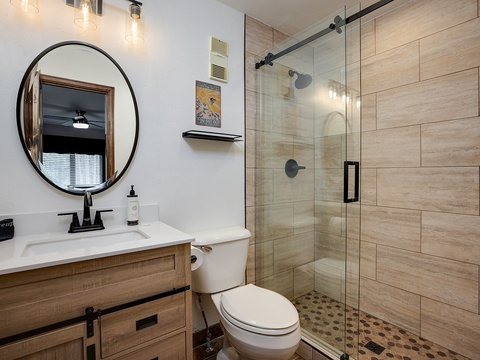 Step into your beautifully designed bathroom featuring wood-tone finishes and a spacious walk-in shower with sleek glass doors—perfect for refreshing after a day exploring.