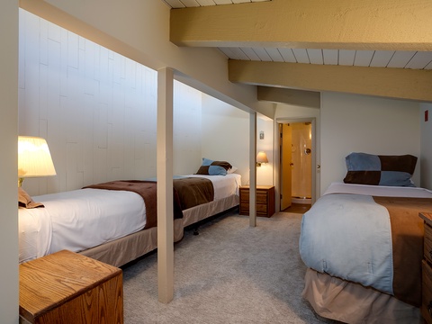 Your group will love this spacious bedroom with three comfortable beds, warm wooden accents, and a cozy carpeted floor—perfect for restful nights after your adventures.
