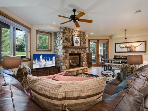 Sink into plush leather seating beside a warm river-rock fireplace. Your open-concept retreat features natural wood accents, high ceilings, and views of the outdoors—perfect for relaxing after a day of adventure.