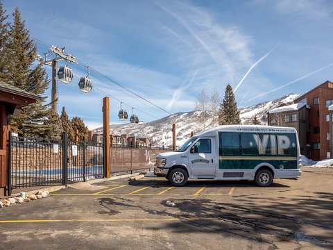 A ski resort shuttle parked at the base, with gondola lifts rising toward snowy mountain slopes—convenient transportation to the slopes.