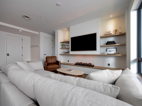 Sink into plush seating in your bright, modern living room, where natural light flows through floor-to-ceiling windows and open shelving adds a personal touch to your urban retreat.