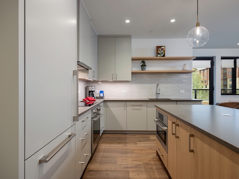 Your spacious modern kitchen features sleek cabinetry, stainless appliances, and all the counter space you need for meal prep, plus views of the surrounding neighborhood through large windows.