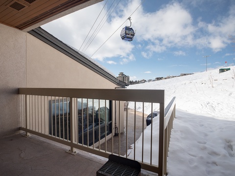 Snow-covered hillside overlooking a ski gondola lift with mountain and winter sports facilities visible in the immediate surroundings.
