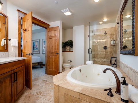 Unwind in your private spa-like bathroom with a deep soaking tub and spacious walk-in shower, all framed by warm wood accents and soft lighting.