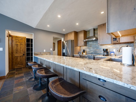 Gather around the expansive granite island with bar seating where you can prep meals, share stories, and enjoy modern appliances in this warm, welcoming kitchen space.