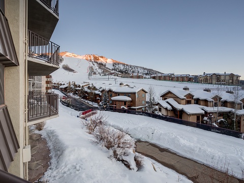 A scenic winter mountain resort village with snow-covered slopes and nearby vacation homes beneath towering alpine peaks under clear skies.