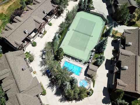 Aerial view captures the property's resort-style amenities: a refreshing swimming pool, hot tub, and tennis court surrounded by mature landscaping and multi-unit vacation homes.
