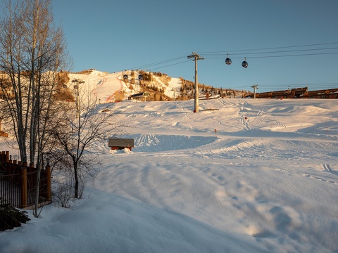 A ski resort area with snow-covered slopes, chair lifts, and nearby lodging, bathed in warm afternoon light during winter season.