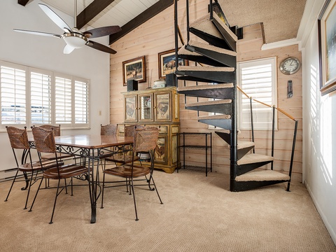 Picture yourself gathered around this inviting dining table, sunlight streaming through plantation shutters, with a charming spiral staircase leading to your cozy loft retreat above.