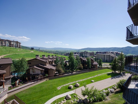 The property is located in a scenic mountain resort community with expansive green lawns, walking paths, and sweeping views of rolling hills and distant peaks.