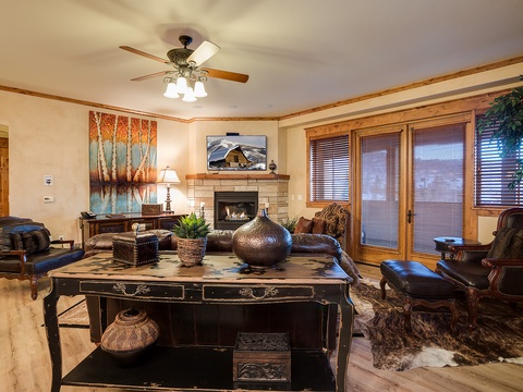 Unwind in your spacious living room with a warm fireplace, stylish leather seating, and a ceiling fan to keep you comfortable. Vibrant artwork and natural light create an inviting space for relaxation.