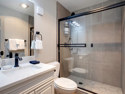Your private bathroom blends style and comfort with elegant neutral tones, a spacious walk-in shower with sleek black framing, and plush towels waiting for your arrival.
