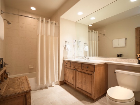 Step into your private bathroom with warm wood vanity, spacious shower-tub combo, and thoughtful touches like plush towels waiting for you after a long day exploring the mountains.