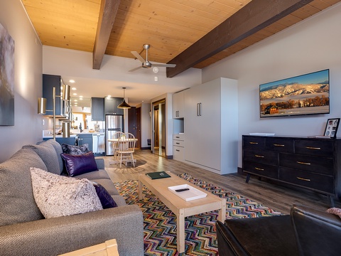 Relax on the plush sofa and unwind beneath vaulted wood-beam ceilings in this inviting open-plan living space with mountain views and modern touches throughout.