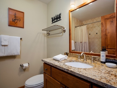 Your private bathroom features warm wood cabinetry, granite countertops, fresh towels, and western-inspired touches that create a cozy, home-away-from-home retreat.