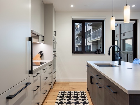 Sleek, modern kitchen with natural light, crisp white countertops, warm wood cabinetry, and stainless steel appliances. The open layout blends style and comfort for creating memorable meals.