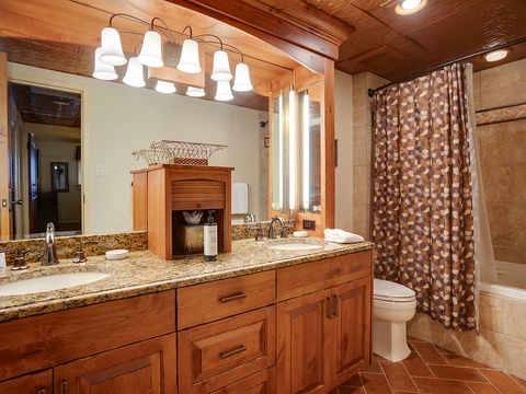 Relax in your spacious bathroom featuring warm wood cabinetry, granite countertops, abundant lighting, and a soothing tub-shower combination perfect for unwinding after mountain adventures.