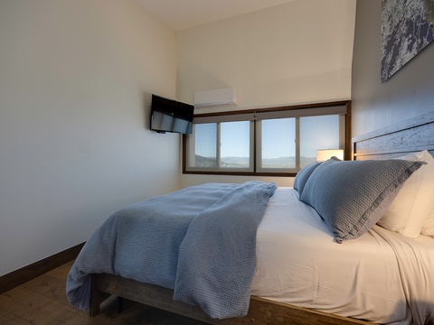 Sink into crisp white linens and cozy textured throws in your peaceful bedroom, where scenic mountain views frame your restful retreat and modern comforts await.