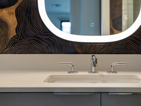 This modern vanity features sleek chrome fixtures, a minimalist sink, and a stunning backlit mirror with contemporary wall detailing—your stylish space to freshen up and feel at home.