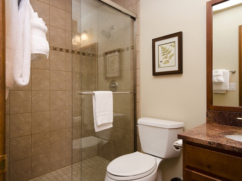 Your private bathroom features warm travertine tile, a sleek glass-enclosed shower, and plush towels ready to wrap you in comfort after a refreshing rinse.