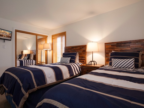 Sink into plush twin beds with rustic wood headboards and crisp nautical linens—your cozy retreat awaits after a day of adventure.