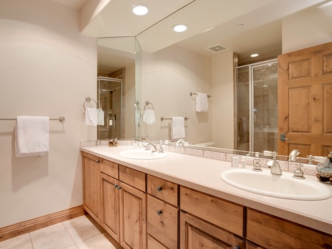 Freshen up in your spacious bathroom with dual sinks, custom cabinetry, and a glass-enclosed shower—pristine white towels and thoughtful touches await you.