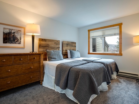 Unwind in your serene bedroom featuring plush bedding, rustic wooden accents, and soft lighting. Two cozy twin beds invite restful nights while natural light fills the space.