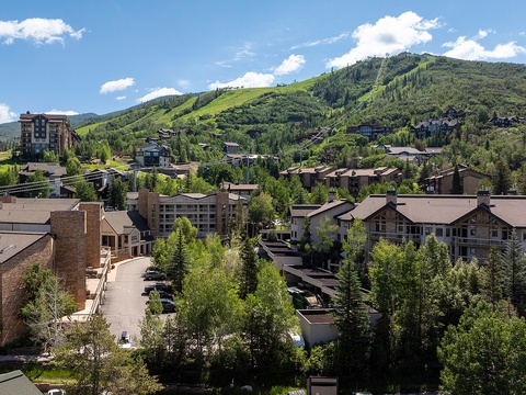 Mountain resort village nestled among evergreens with lush green ski slopes rising in the background, offering year-round outdoor recreation and scenic alpine beauty.