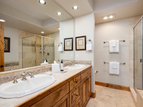 Your spacious bathroom features dual vanities, a walk-in shower with elegant tile work, and plush white towels waiting for you. Warm wood cabinetry adds a touch of mountain charm to your daily routine.