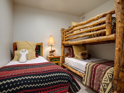 Relax in this cozy bedroom featuring rustic log bunk beds and a comfortable full-size bed, adorned with warm Southwestern blankets and charming woodland accents.