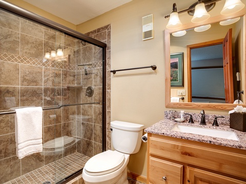 Your private bathroom features a spacious tiled walk-in shower, elegant granite countertop, and warm wood finishes—everything you need to refresh after a day of adventure.