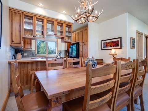 Gather around this handcrafted wooden table beneath a stunning antler chandelier, where your family meals become cherished mountain memories in this warm, open kitchen and dining space.
