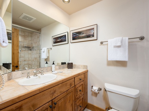 Warm wood cabinetry and natural stone countertops create a welcoming bathroom retreat. Fresh towels and thoughtful amenities ensure your comfort throughout your stay.