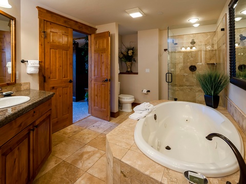 Unwind in your private spa-like bathroom featuring a luxurious jetted tub and spacious walk-in shower with elegant travertine tile, warm wood cabinetry, and serene touches throughout.