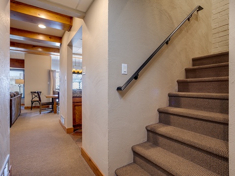 Step into your spacious retreat, where warm wooden beams and cozy carpeted stairs lead you to comfortable living areas designed for your relaxation and mountain getaway.