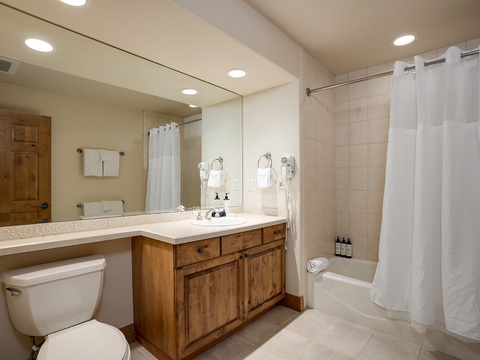 Refresh in your private bathroom featuring a spacious vanity, tiled shower-tub combo, and cozy wood-toned accents that make every morning feel like a retreat.