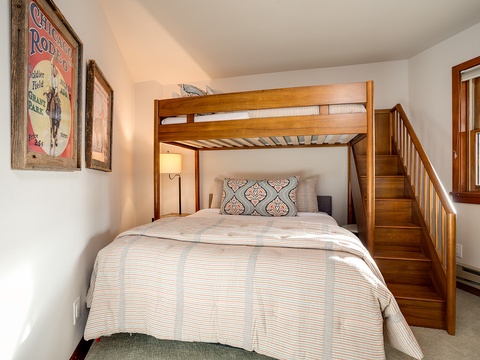 Your cozy bedroom features a queen bed beneath a twin loft bunk, perfect for families or groups. Warm wood tones and vintage decor create a welcoming mountain retreat.